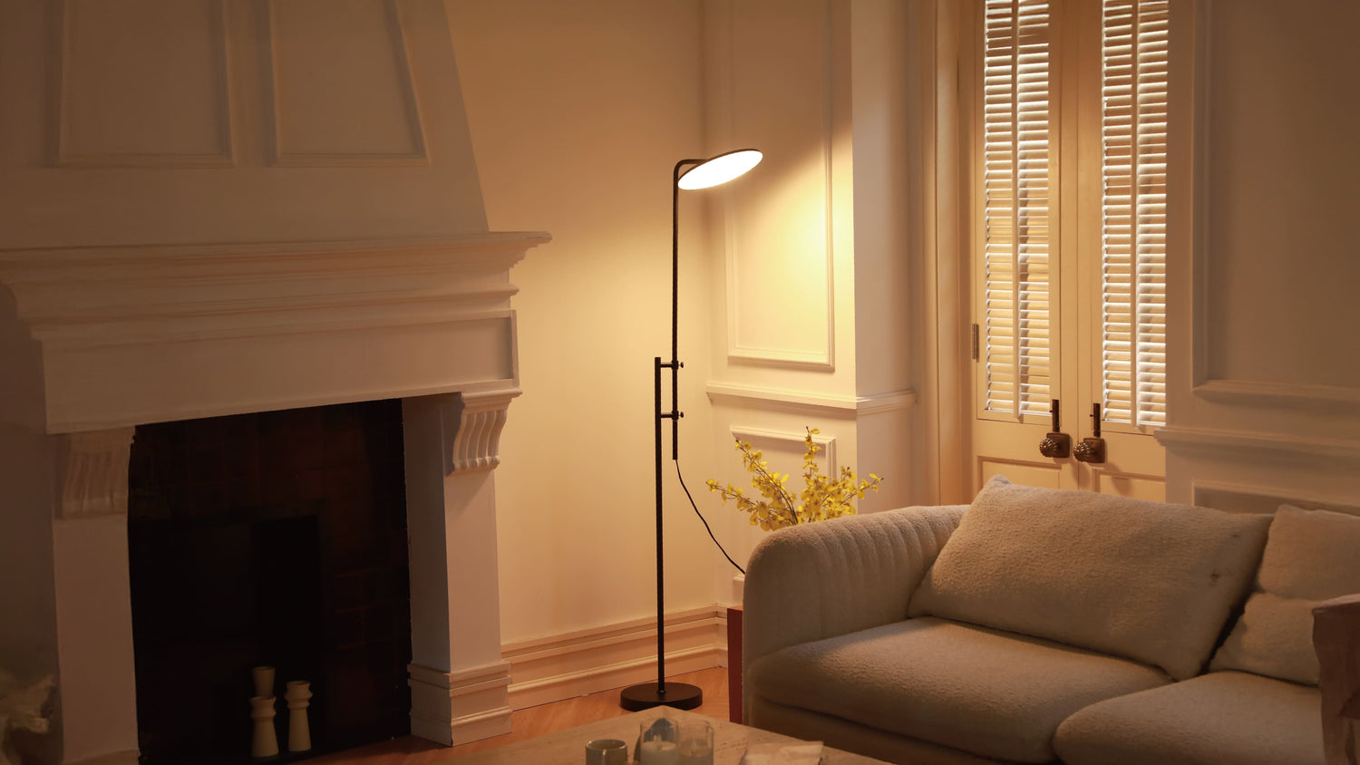 A modern floor lamp with a gold finish placed in a cozy living room corner next to a green armchair, casting a warm glow.