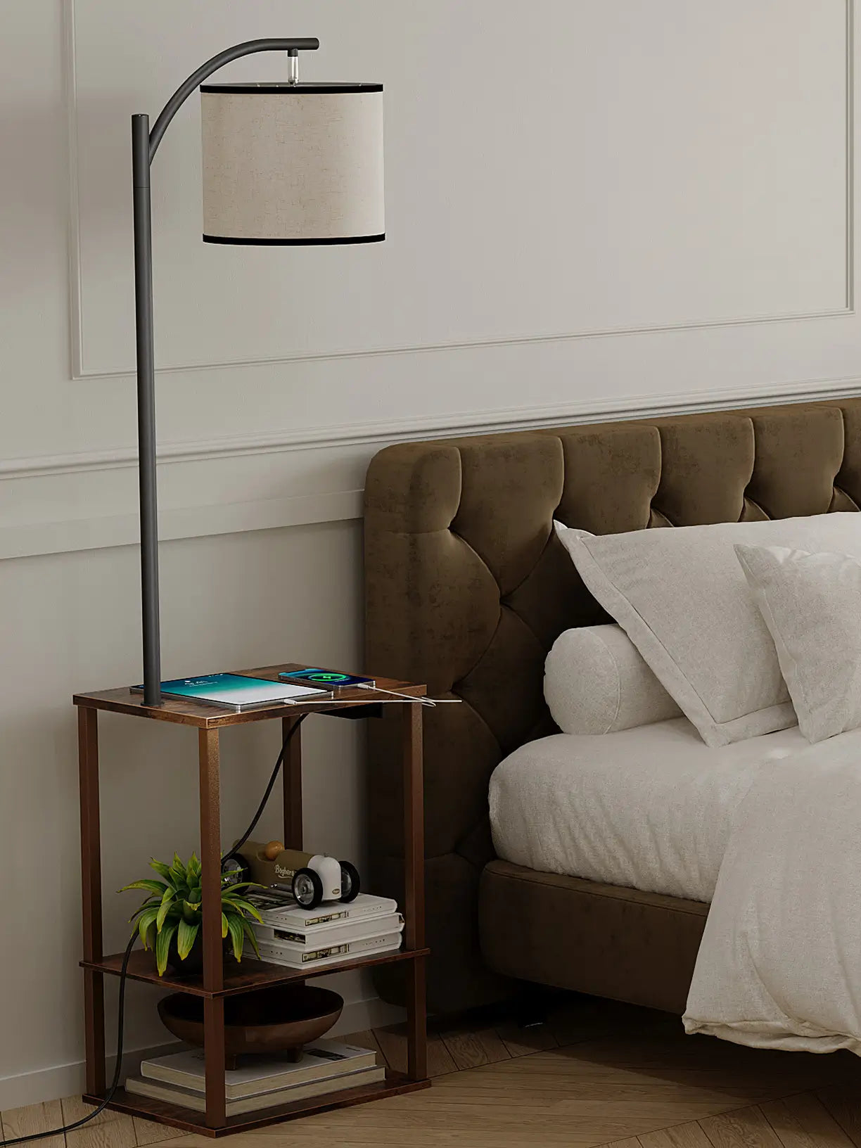 A stylish bedside floor lamp featuring a built-in three-tier side table, offering convenient storage and charging for a smartphone, positioned next to a plush brown bed in a modern bedroom.