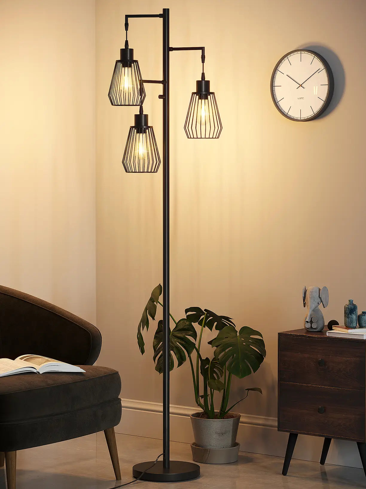 A sleek black cage 3-head floor lamp with exposed bulbs, offering stylish multi-directional lighting in a modern living space with a large green fiddle-leaf fig plant and a patterned rug.