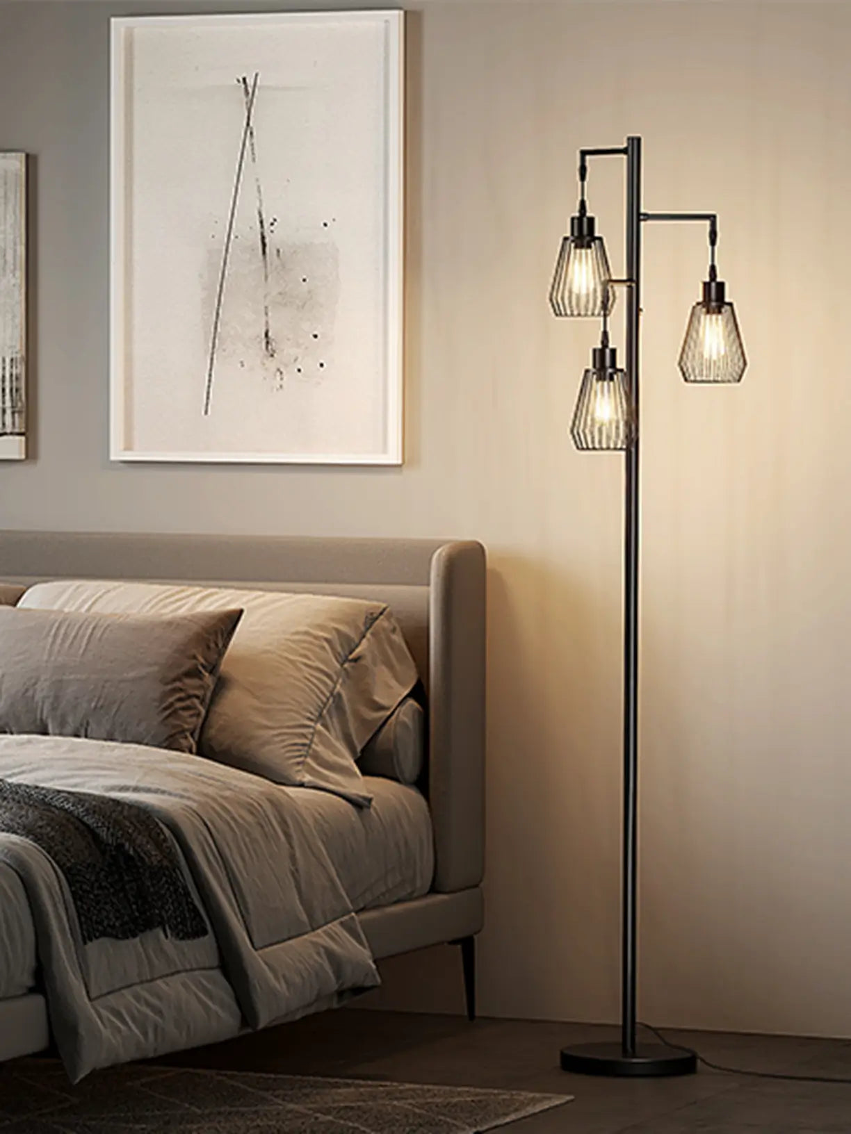 A modern farmhouse style 3-light floor lamp with black metal cage shades and Edison bulbs, providing warm ambient lighting in a cozy bedroom with a large bed and framed artwork.