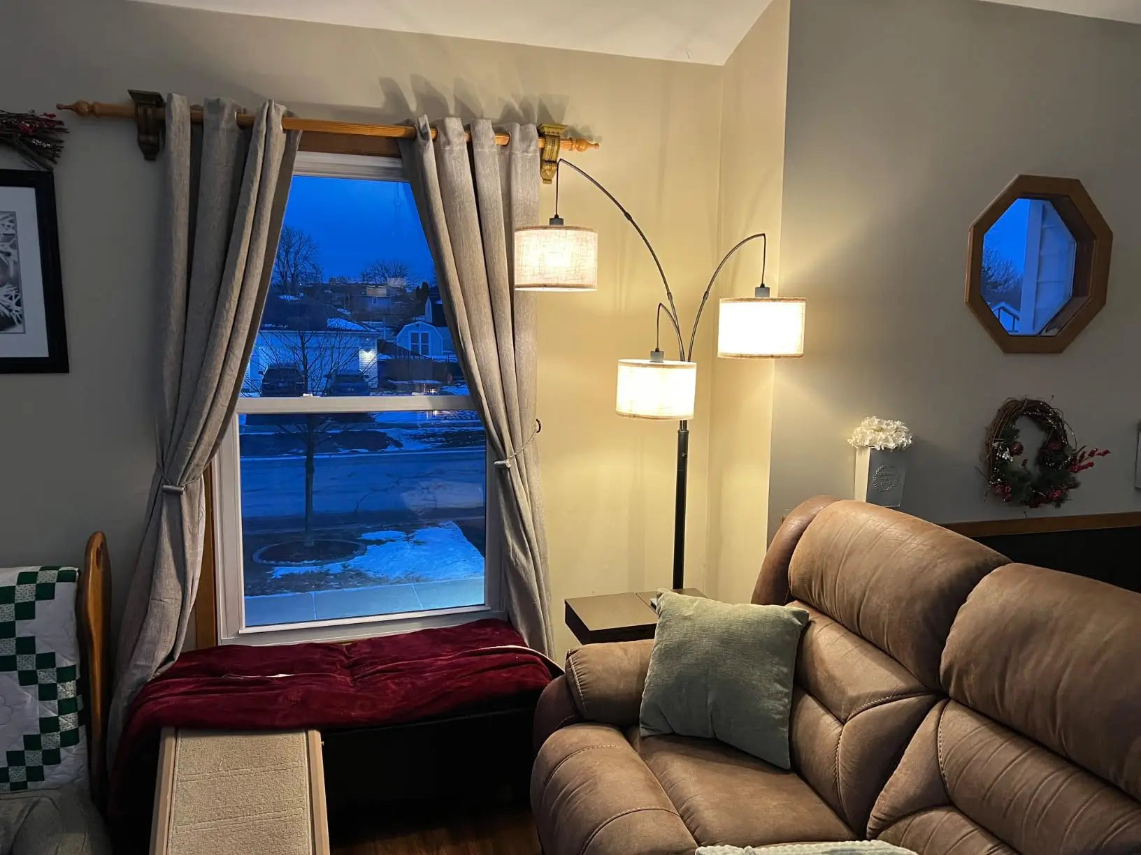 A modern three-arm arc floor lamp with light drum shades illuminating a cozy living room with a sectional sofa and a small side table.