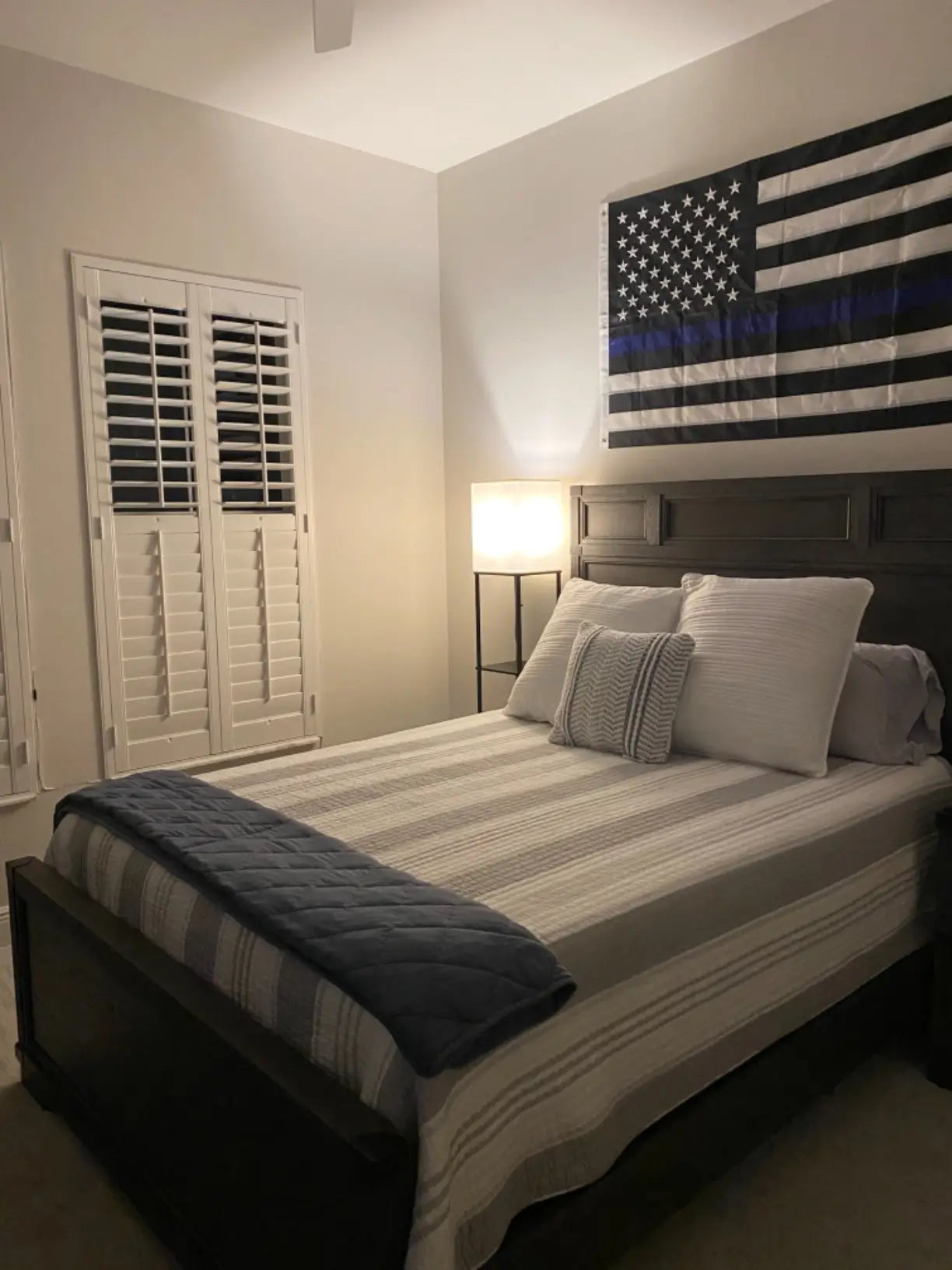 A sleek, minimalist black floor lamp with a shade head, serving as an excellent reading light beside a modern bed in a cozy bedroom.
