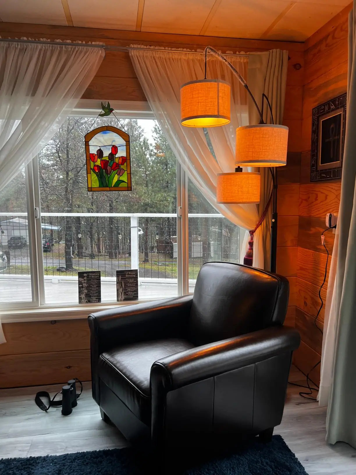 A contemporary tree-arm floor lamp with three fabric shades casting light over a comfortable armchair and a side table in a decorated living area with wall art.