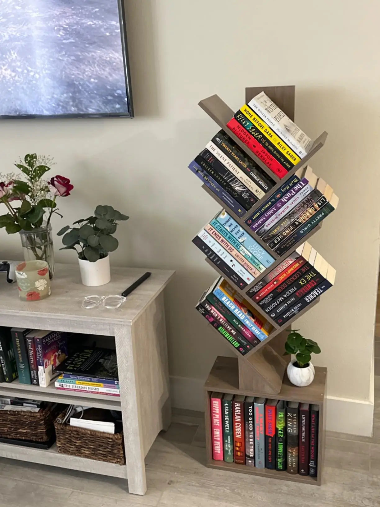 A contemporary tree bookshelf with a sturdy and stable base, supporting several "branches" of shelving, neatly arranged with various books and small objects.