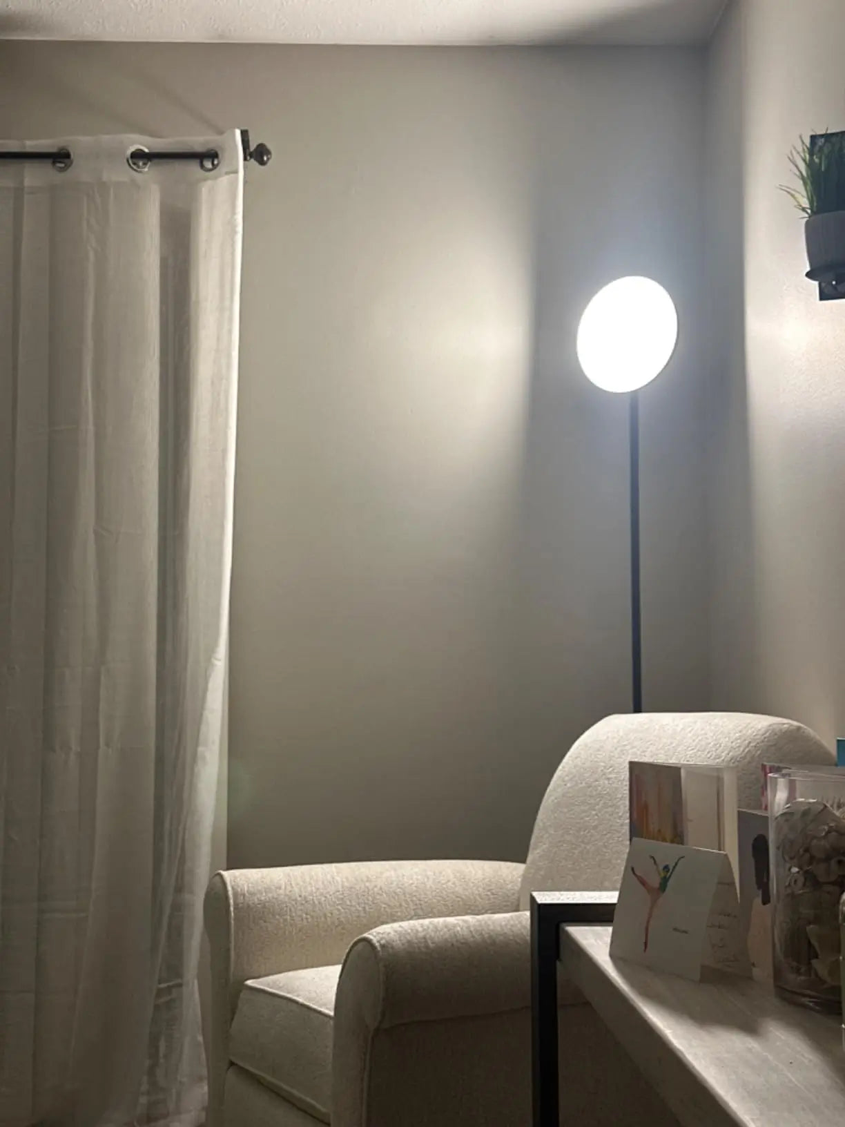 A modern torchiere floor lamp with a dark finish and an upward-facing light, positioned in a cozy corner of a room, ideal for providing ambient lighting for reading or general illumination.