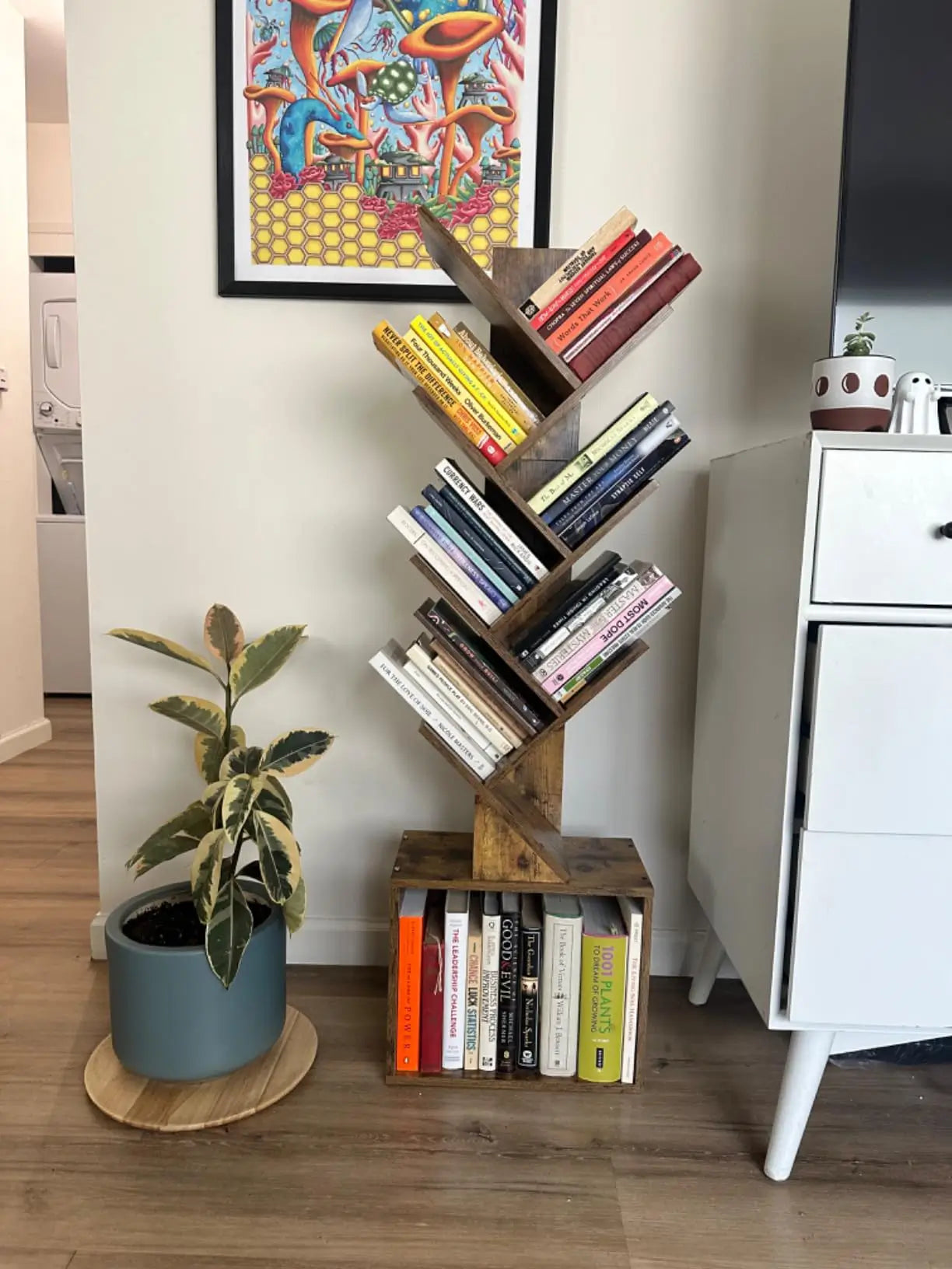 A decorative tree bookshelf serving as a charming corner accent in a home, with its multiple "branches" holding a collection of books and small plants.