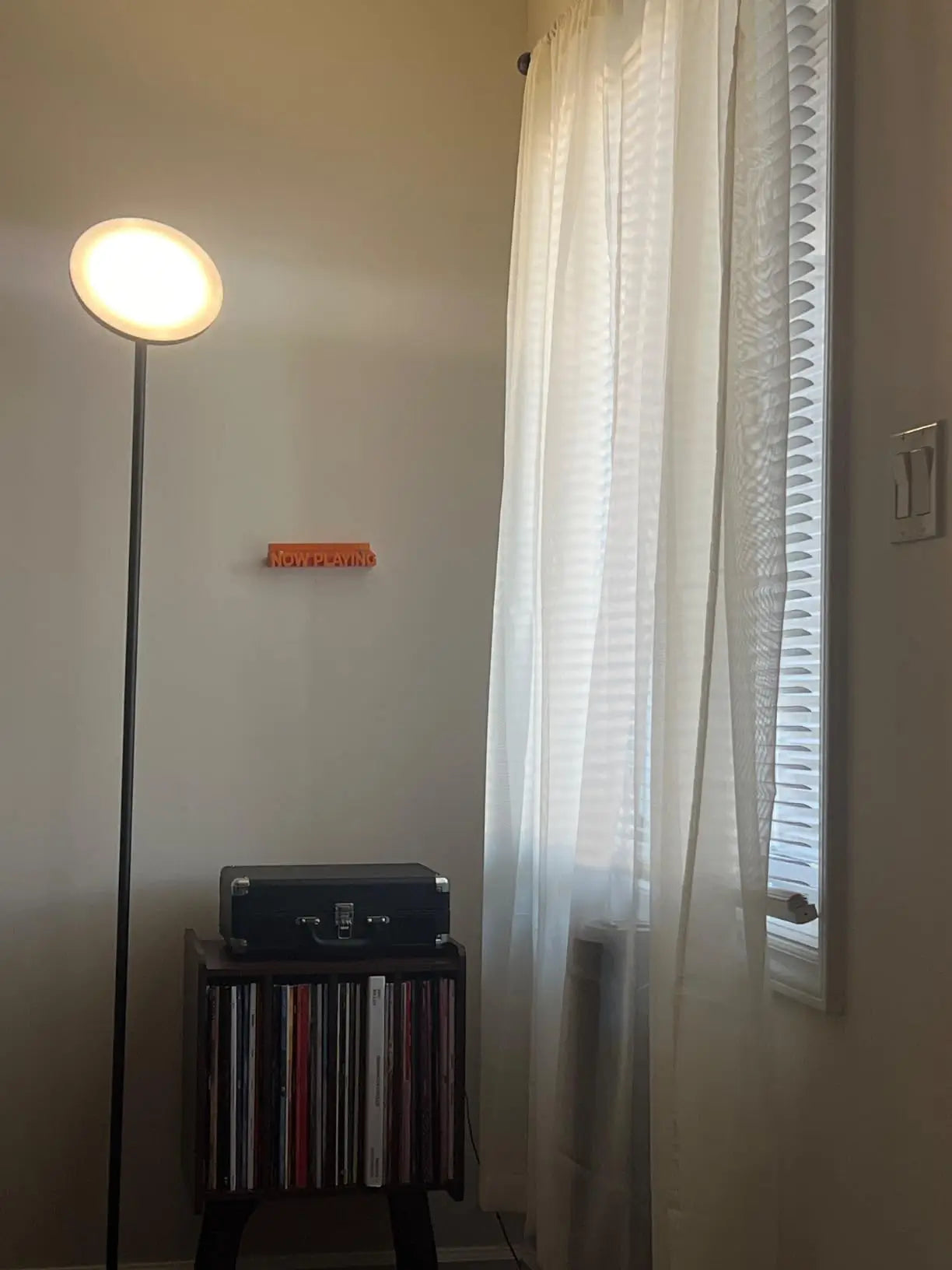 A minimalist black torchiere floor lamp with a slender design and an upward-facing integrated light, providing soft ambient illumination in a modern bedroom setting with a bed and a simple side table.