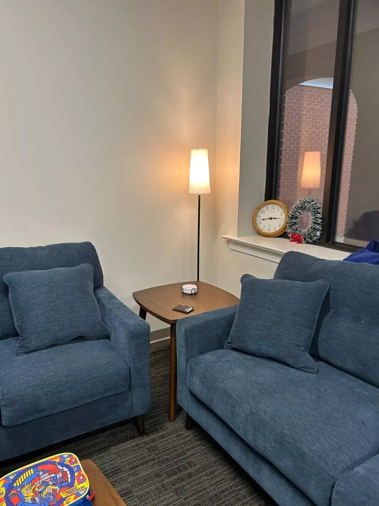 Minimalist floor lamp with soft white shade placed between two blue sofas in a modern living room setting