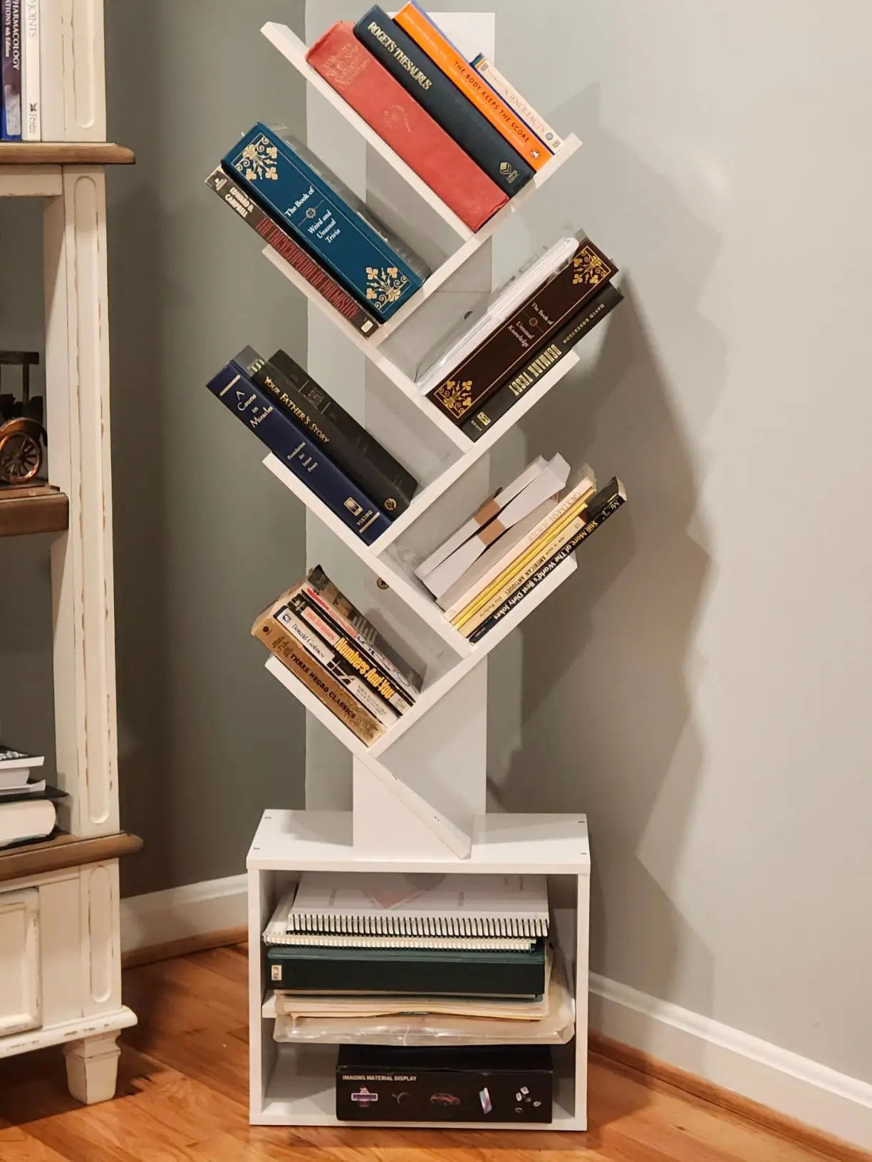 A minimalist white tree bookshelf with a sleek, compact design, offering vertical storage for books and decorative items, ideal for small spaces or modern interiors.