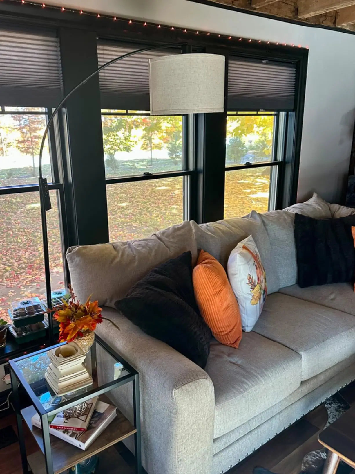 A sleek, modern arched floor lamp with a metal base and a large white fabric shade, positioned to provide overhead lighting for a contemporary gray sectional sofa in a living room.
