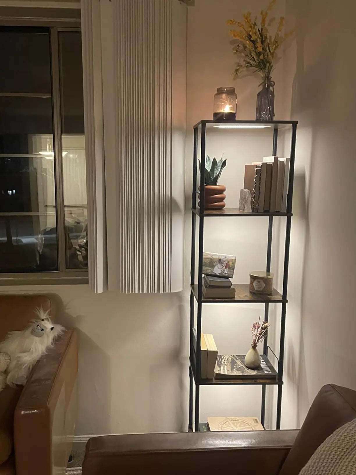 A modern display shelf with multiple tiers, featuring integrated adjustable LED lights illuminating a collection of books and decorative items, ideal for a living room or study.