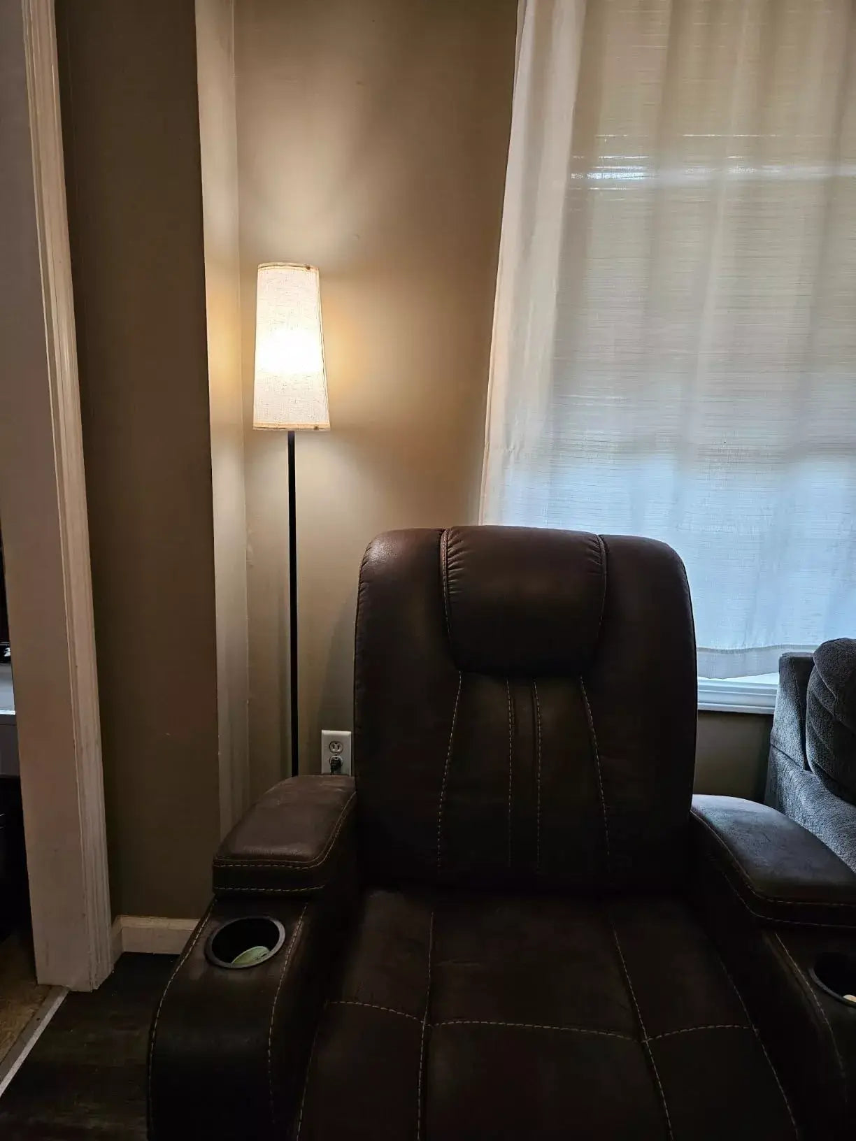 Modern floor lamp with beige lampshade next to a brown leather recliner in a cozy reading corner