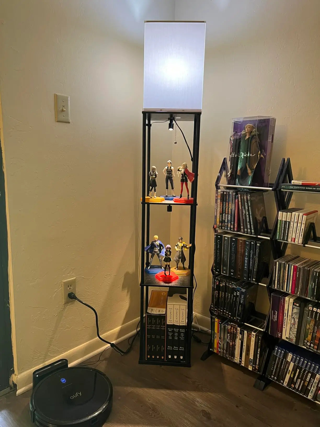 A modern floor lamp with a dark, slender stand and a minimalist square shade, providing light over a display shelf in a contemporary living room.