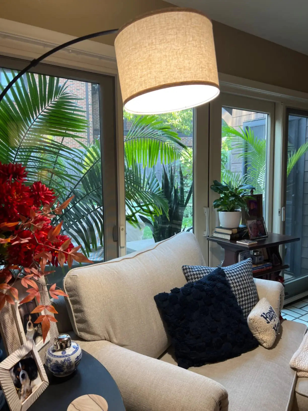 A modern minimalist arc floor lamp with a thin dark stand and a unique, light-colored wooden-textured shade, illuminating a small side table and a cozy seating area in a living room.