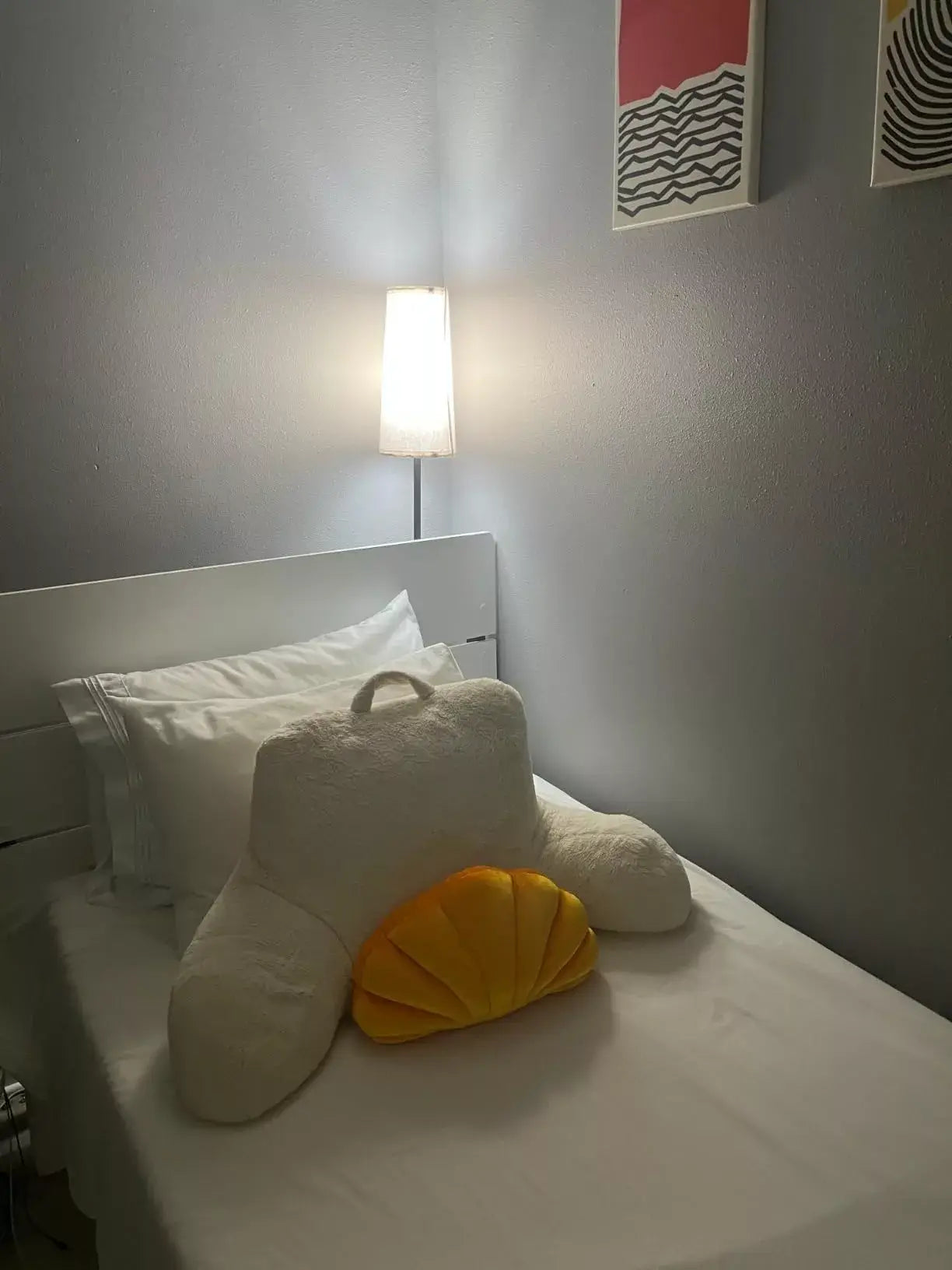 A sleek white floor lamp illuminating a cozy bedroom corner, providing ambient lighting and a modern touch to the space.