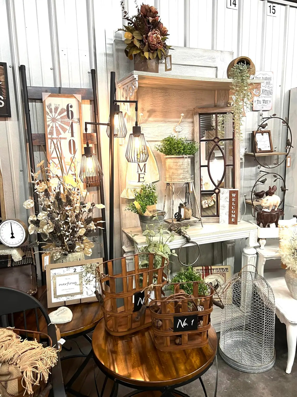 A rustic industrial 3-bulb floor lamp with black wire cage shades, providing task lighting in a home office or study corner with a wooden desk and a comfortable chair.