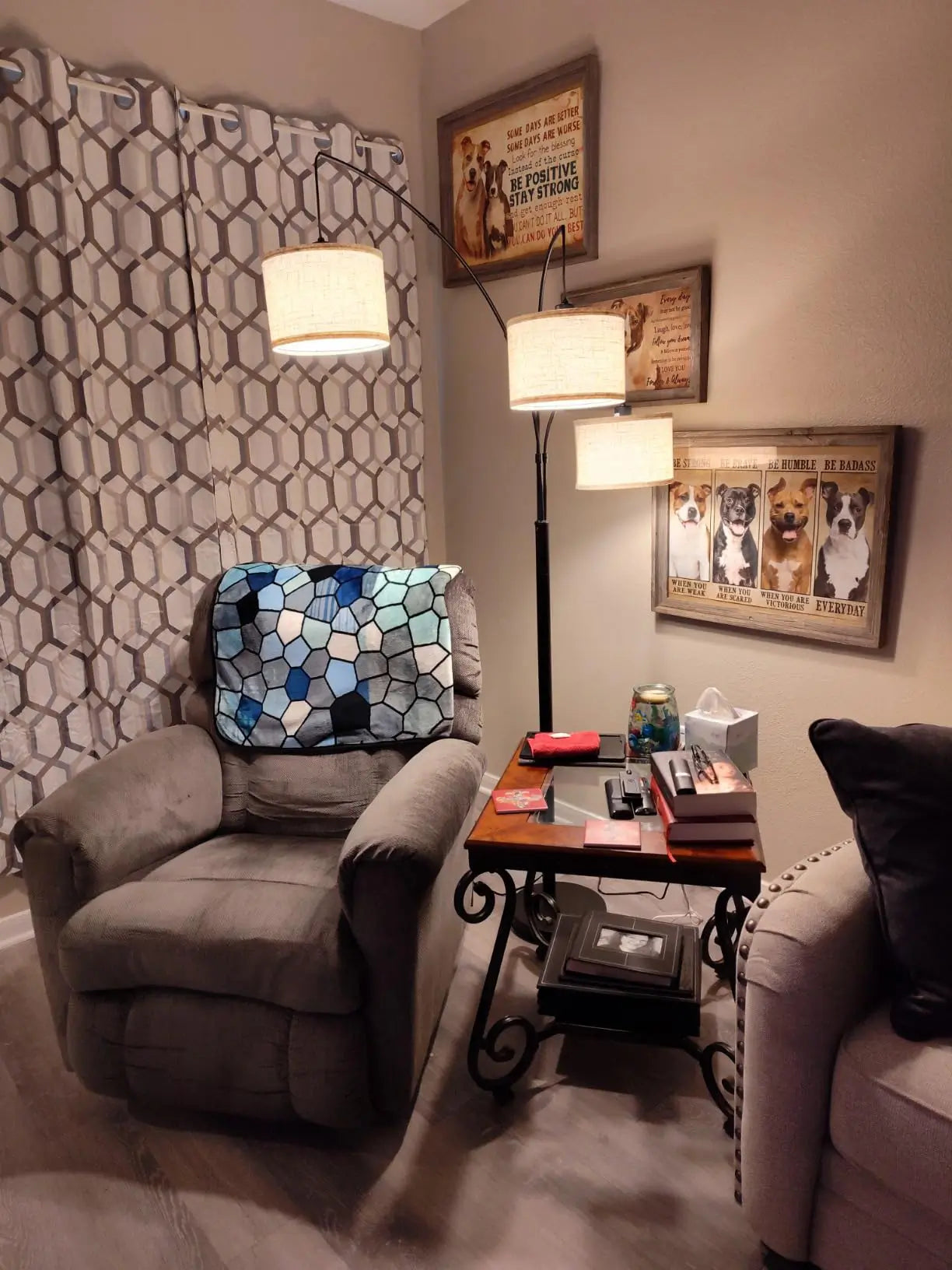 A rustic three-shade arc lamp with amber-toned drum shades in a wood-paneled cabin, illuminating a leather armchair near a window with a stained glass accent.